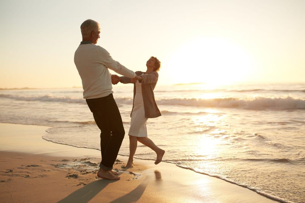 Older man and woman at sunset holding each other's hands in the waves of the ocean