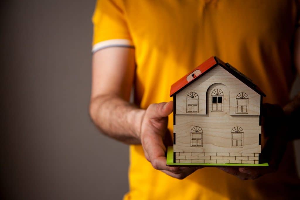 Man in yellow shirt holding wooden model of house