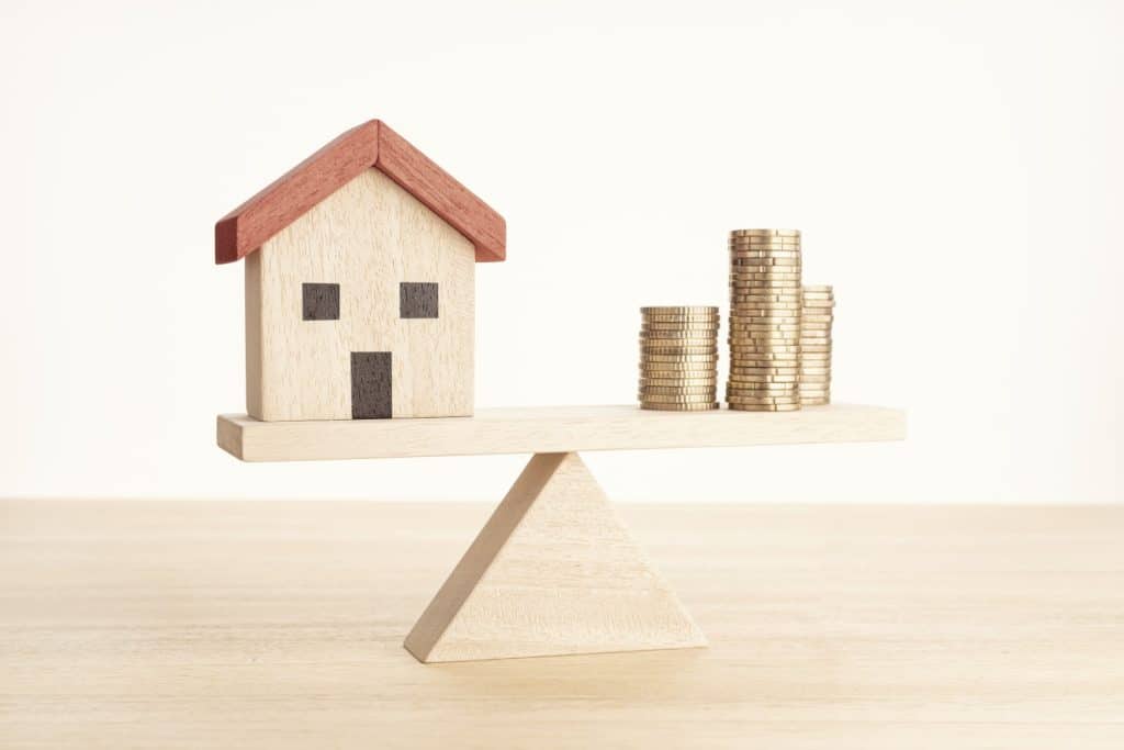 wooden toy house and stack of coins on balancing scale