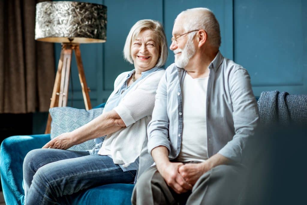 senior married couple smiling while sitting on couch