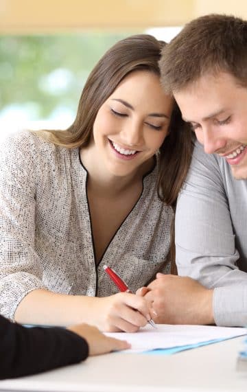 A smiling young couple signing the paperwork to buy their first home
