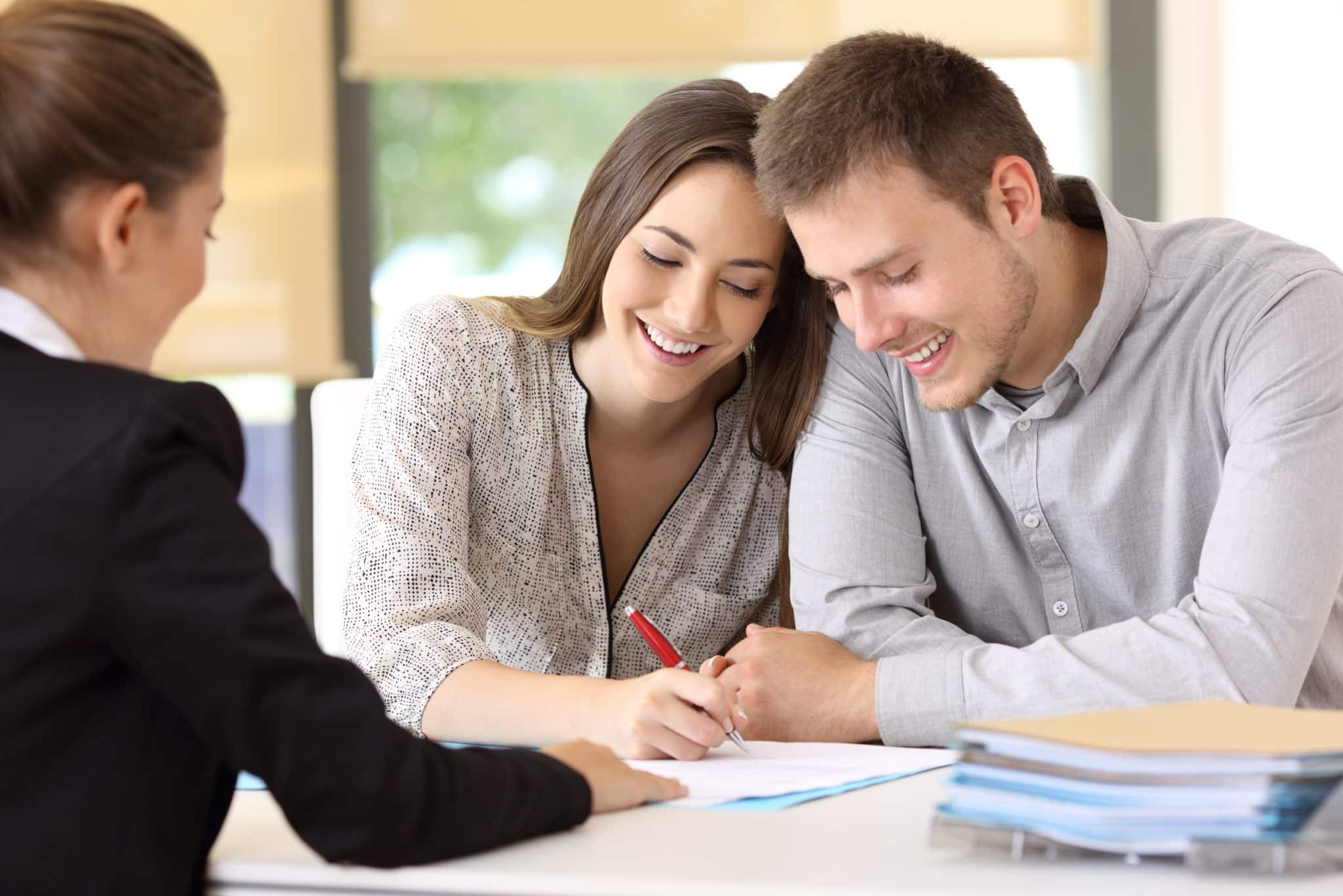 A smiling young couple signing the paperwork to buy their first home